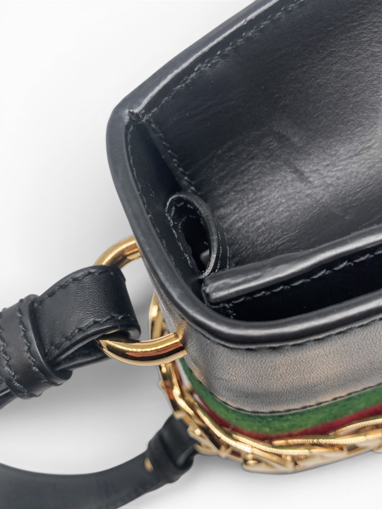 Detailed view of Gucci Sylvie black leather bag hardware, showcasing the top handle connection, gold-tone fittings and iconic web stripe From luxury designer consignment boutique, Dee Black. In Perth, Western Australia.